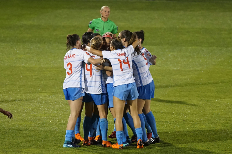 Soccer players huddled together on a field with a NWSLsoccer.com banner in the background.